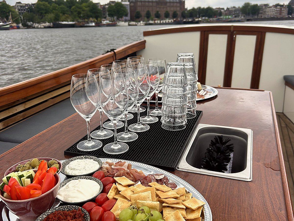 Borrelplank met dips, olijven, tomaatjes en druiven op de tafel aan boord, met de Amsterdamse skyline op de achtergrond